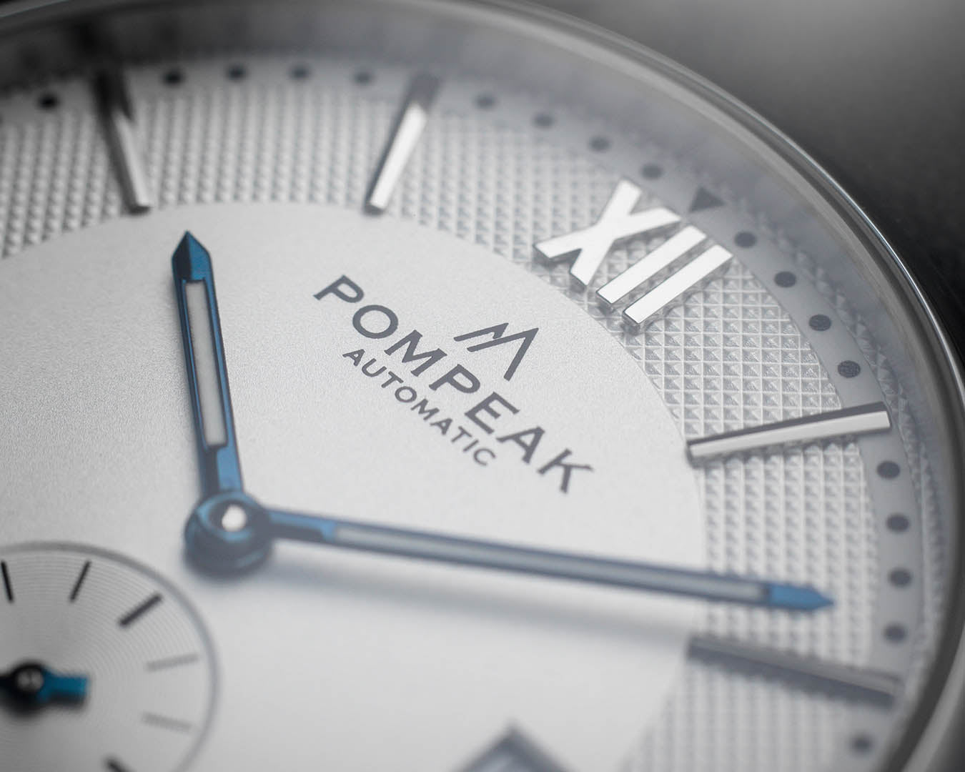 Close-up of the Mallory Timeless White watch dial, featuring a printed logo, heat-blued hands, applied Roman numeral indices, and a textured finish.