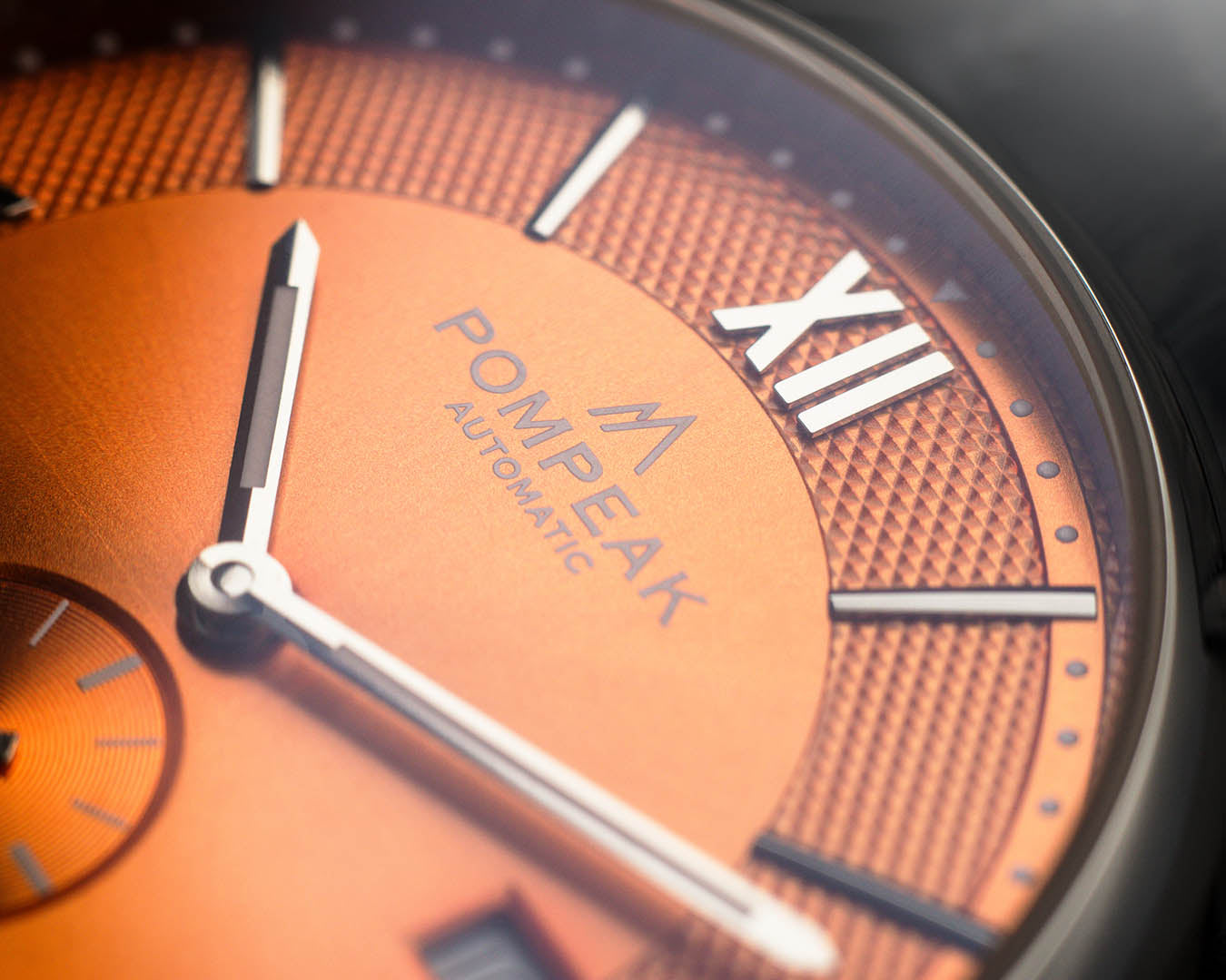Close-up of the Mallory Orange Crush watch dial, featuring a printed logo, polished silver hands, applied Roman numeral indices, and a textured finish.