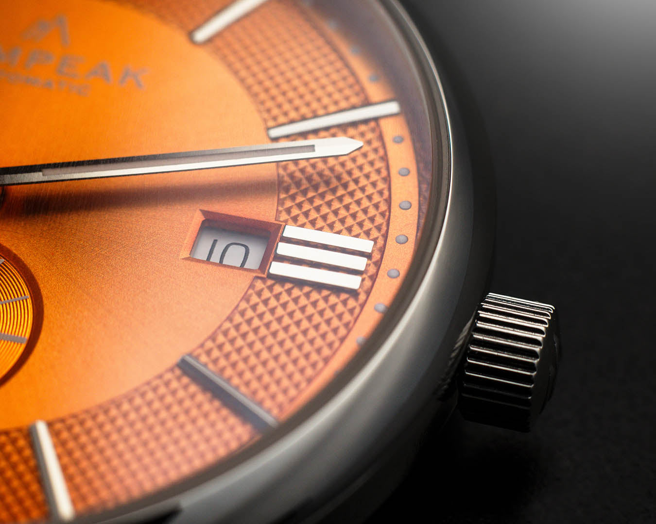 Detailed view of the Mallory Orange Crush watch dial, showing the date window, polished silver hands, applied indices, textured finish, and signed crown.