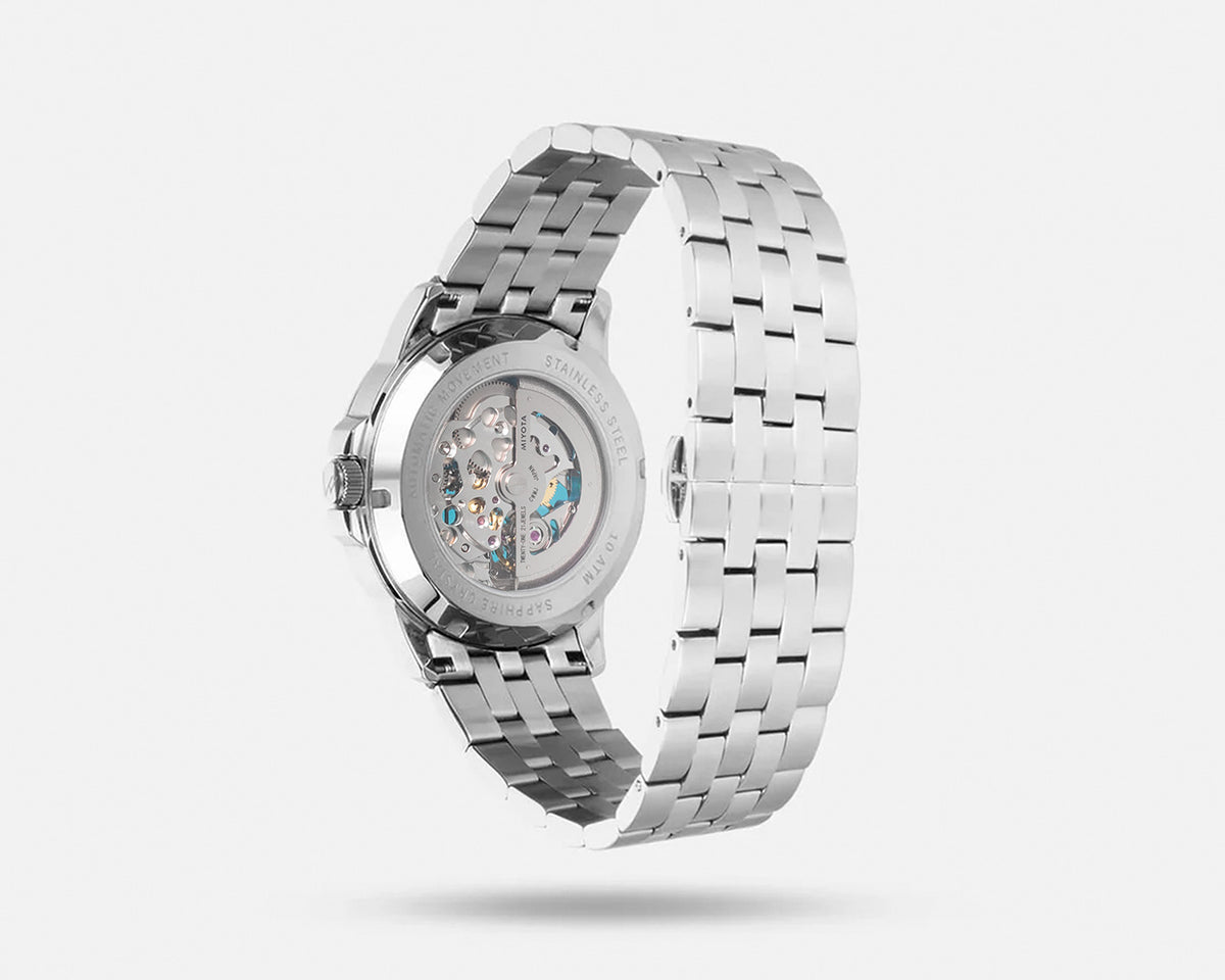 Silver stainless steel automatic watch with a transparent case back showing the mechanical movement, displayed on a light gray background.
