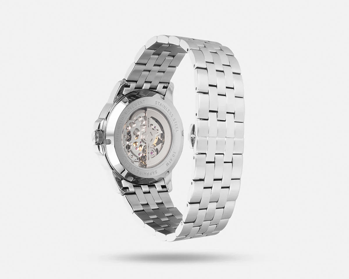 Silver stainless steel automatic watch with a transparent case back showing the mechanical movement, displayed on a light gray background.